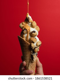 A Hand Holding An Ice Cream Cone Topped With Cookie Dough Bites While Caramel Sauce Is Streaming Down From The Top Of The Frame