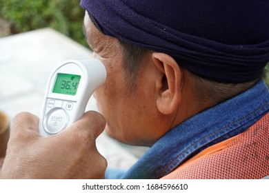 Hand Holding Infrared Thermometer To Measuring Temperature On  The Side Of The Face Of The Worker Before Entering The Chemical Industrial Plant In Construction Area. Covid Flu Screening 19 Concept.