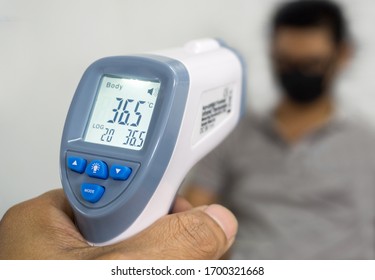 Hand Holding Infrared Thermometer To Measuring Temperature On Blurred Asia People With Face Mask On Background. Covid Flu Screening 19 Concept.