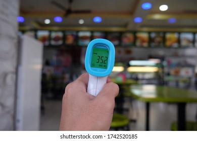 Hand Holding Infrared Thermometer With Restaurant Background.