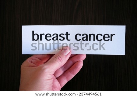 Hand holding the inscription breast CANCER on the paper on black wooden background, closeup, concept