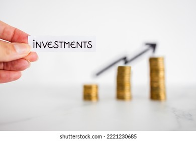 hand holding Investment text in front of growing stacks of coins with arrow pointing upward, metaphor of increasing your savings and compound interests