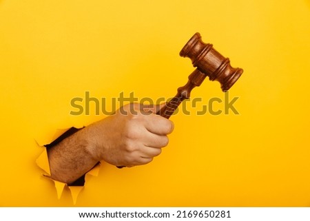 Hand holding a judge's gavel through torn yellow background. Law and auction aconcept.