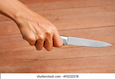 Hand Holding Knife Against Plank Wood
