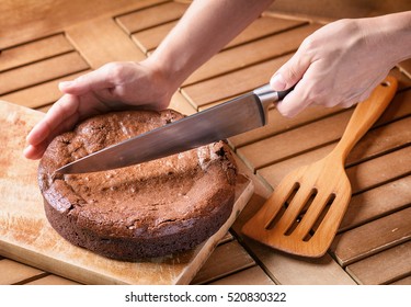 Hand Holding Knife And Cutting Freshly Baked Brownie Cake On Wooden Table. Homemade Delicious Sweet Chocolate Dessert, Family Meal.