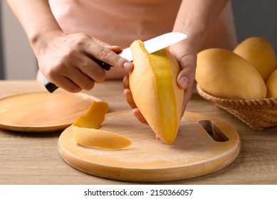 Hand holding knife and peeling Thai mango fruit (Nam Dok Mai) on wooden board, Tropical fruit in summer season - Powered by Shutterstock