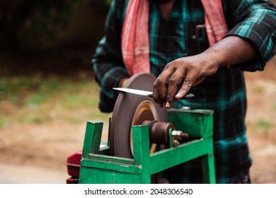 Hand holding a knife and sharpening it on a sharpening wheel. Metal blade sharpening machine in action. Local service in India - Powered by Shutterstock