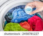 Hand holding laundry detergent with colorful clothes in washing machine