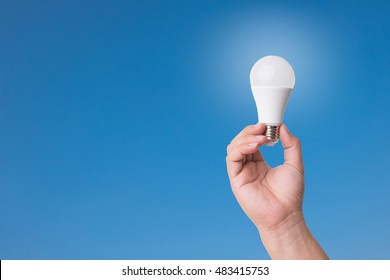 Hand holding LED Bulb with Lighting on blue sky background. Eco power concept.