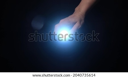 A hand holding a led flashlight with blue beam and shine in camera in the dark