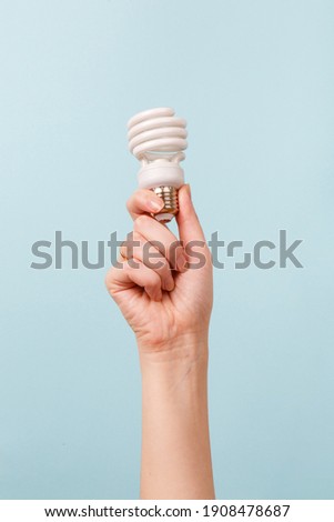 Hand holding a LED light bulb on blue background. Using economical and environmentally friendly light bulb concept. Idea. Energy saving lamp in woman's hand