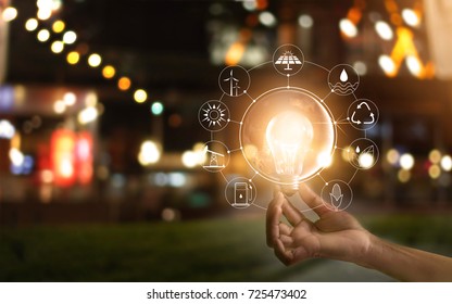 Hand holding light bulb in front of global show the world's consumption with icons energy sources for renewable, sustainable development. Ecology concept. Elements of this image furnished by NASA. 