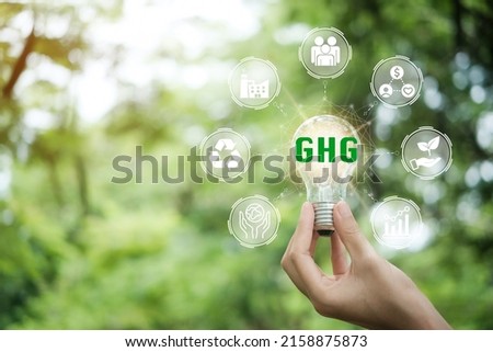 Hand holding light bulb with 'GHG, greenhouse gas’ on a beautiful green background. Business and GHG concept. Copy space. Greenhouse gas symbol. 