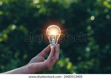 Hand holding a light bulb, green leaf background, natural energy and environment concept.