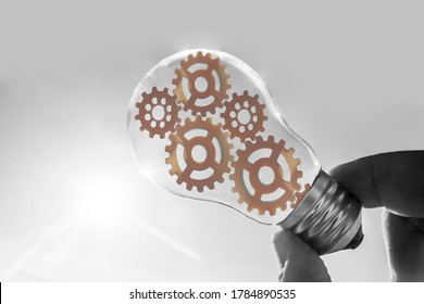 Hand holding light bulb and Innovation gears connection icon inside. Idea and inspiration on white background. sunlight. solar power concept.Bulb With Cogwheels Inside. brainstorming and teamwork idea