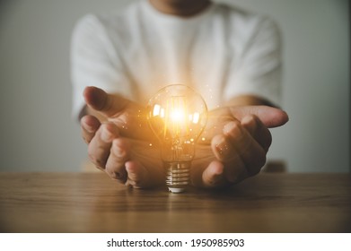Hand holding light bulb on wood table. Concept of inspiration creative idea thinking and future technology innovation - Shutterstock ID 1950985903
