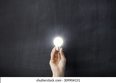 Hand Holding Light Bulb On Blackboard