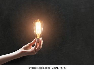 Hand Holding Light Bulb On Blackboard Background 