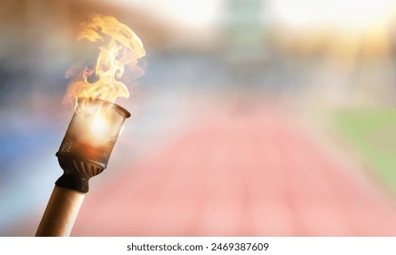 Hand holding lit torch with athletics stadium behind a sunny day. - Powered by Shutterstock