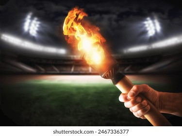 Hand holding lit torch with stadium behind with lights at night. Front view.