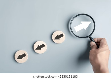 Hand holding magnifier focus to White arrow and different direction facing opposite direction with black arrow for business disruption and technology transformation and different thinking idea