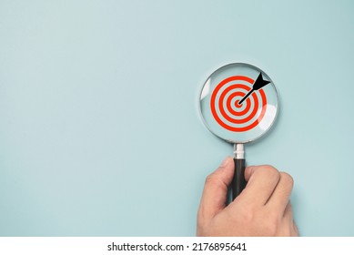 Hand holding magnifier glass with dartboard with arrow for focus and setup business objective target and goal concept. - Shutterstock ID 2176895641