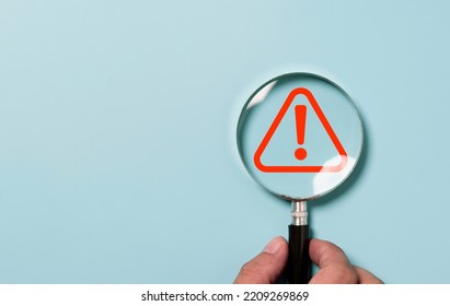 Hand holding magnifier glass with red triangle caution warning sign for focus notification error and maintenance concept.