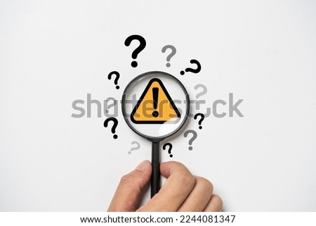 Hand holding magnifier glass with yellow triangle caution warning sign and question mark for notification error and maintenance concept.