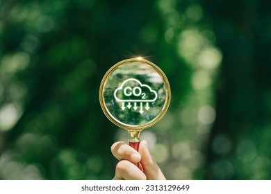 hand holding magnifying glass with CO2 reduction icon inside.A clean and friendly environment without carbon dioxide emissions.carbon credit to limit global warming from climate change.carbon neutral. - Shutterstock ID 2313129649