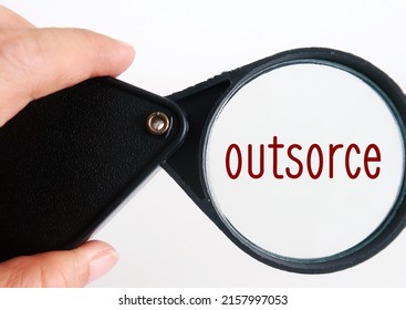 Hand holding magnifying glass focus on words OUTSOURCE, concept of business getting work done by making a contract hiring another company, to send away work to people outside