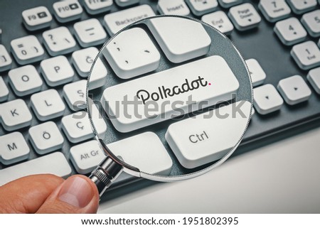 Hand holding magnifying glass and focusing computer key with Polkadot| Dot altcoin logo. Cryptocurrency mining, trading, market concept.
