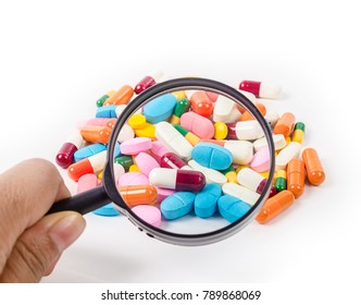 Hand Holding Magnifying Glass With Medicine Pills On White Background.