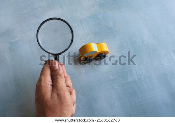 Hand holding magnifying glass\
and toy car. Car inspection, search, looking for car\
concept.