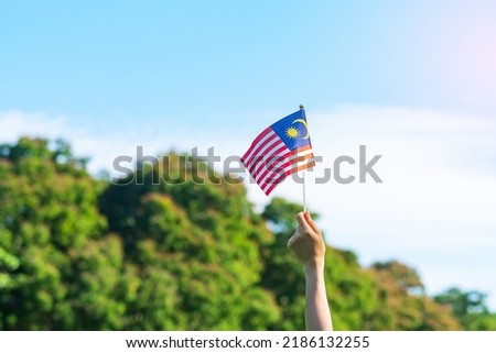 hand holding Malaysia flag on blue sky background. September Malaysia national day and August Independence day