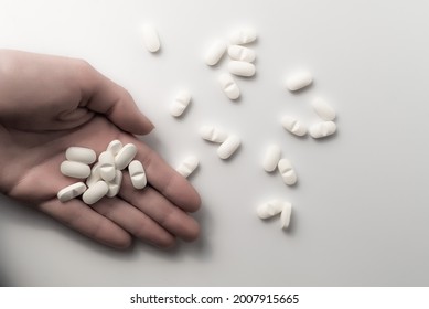 Hand Holding Many Dosages Of Chemical Opioids Medical Pills And A Pile Of Pharmaceutical Medication On Clean White Background With Copyspace - Concept Of Abuse Addiction, Antibiotic Or Healthcare.