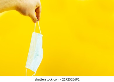 A Hand Holding A Medical Protective Mask On A Yellow Background. Virus Protection. An Epidemic.