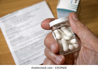 Hand Holding A Medicine Bottle With Pills, Medical Direction Paper And Medicine Box On The Table In The Background