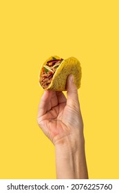 Hand holding a Mexican taco on yellow background