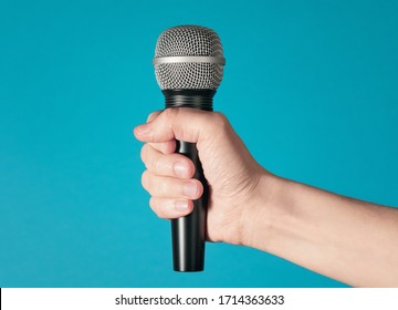 Hand holding up a microphone isolated against a bright blue background 