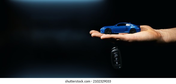 hand holding miniature automobile model and key on dark background. car buying and rental. banner