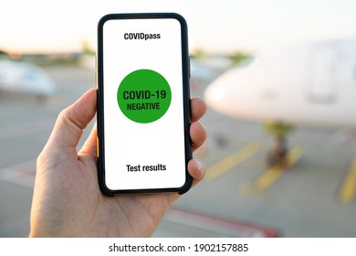 Hand Holding Mobile COVID-19 App For Test Results. Covid Pass For Traveling. Travel Concept. Phone In Airport And Airplane In The Background