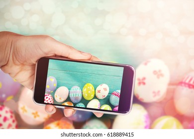 Hand holding mobile phone against white background against painted easter eggs on wooden surface - Powered by Shutterstock