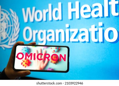 Hand Holding Mobile Phone With Omicron COVID 19 Variant Strain In Front Of Flag Of World Health Organization WHO Showing News App Notification