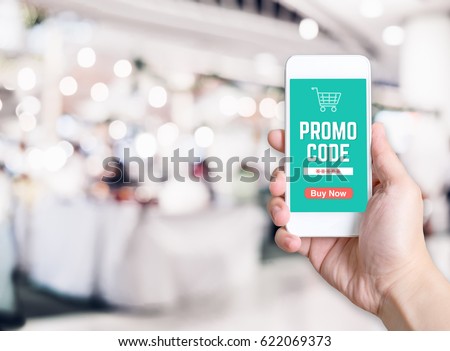 Hand holding mobile phone with promo code word with blurred store background with bokeh light ,internet marketing concept,E-commerce