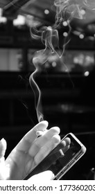 Hand Holding A Mobile Phone And Smoking Cigarette In Black And White.