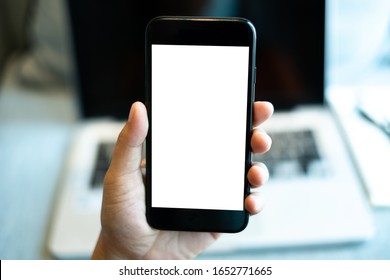 hand holding a mobile phone with white blank screen over the laptop