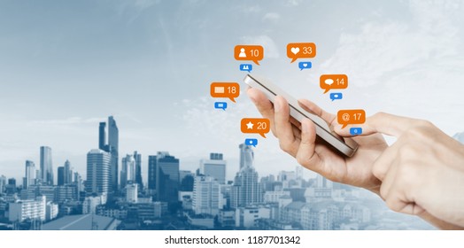 Hand Holding Mobile Smart Phone, With Notification Icons And City Background