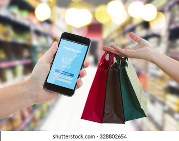 hand holding mobile smart phone with cyber mobile shop  on super market blur background and shopping bags - e-commerce and cyber  retail  marketing concept