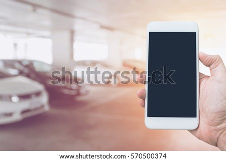 Hand holding mobile smart phone with blank screen, concept of indoor car parking.
