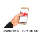 A hand holding mobile smartphone with CNN logo on screen against white background 